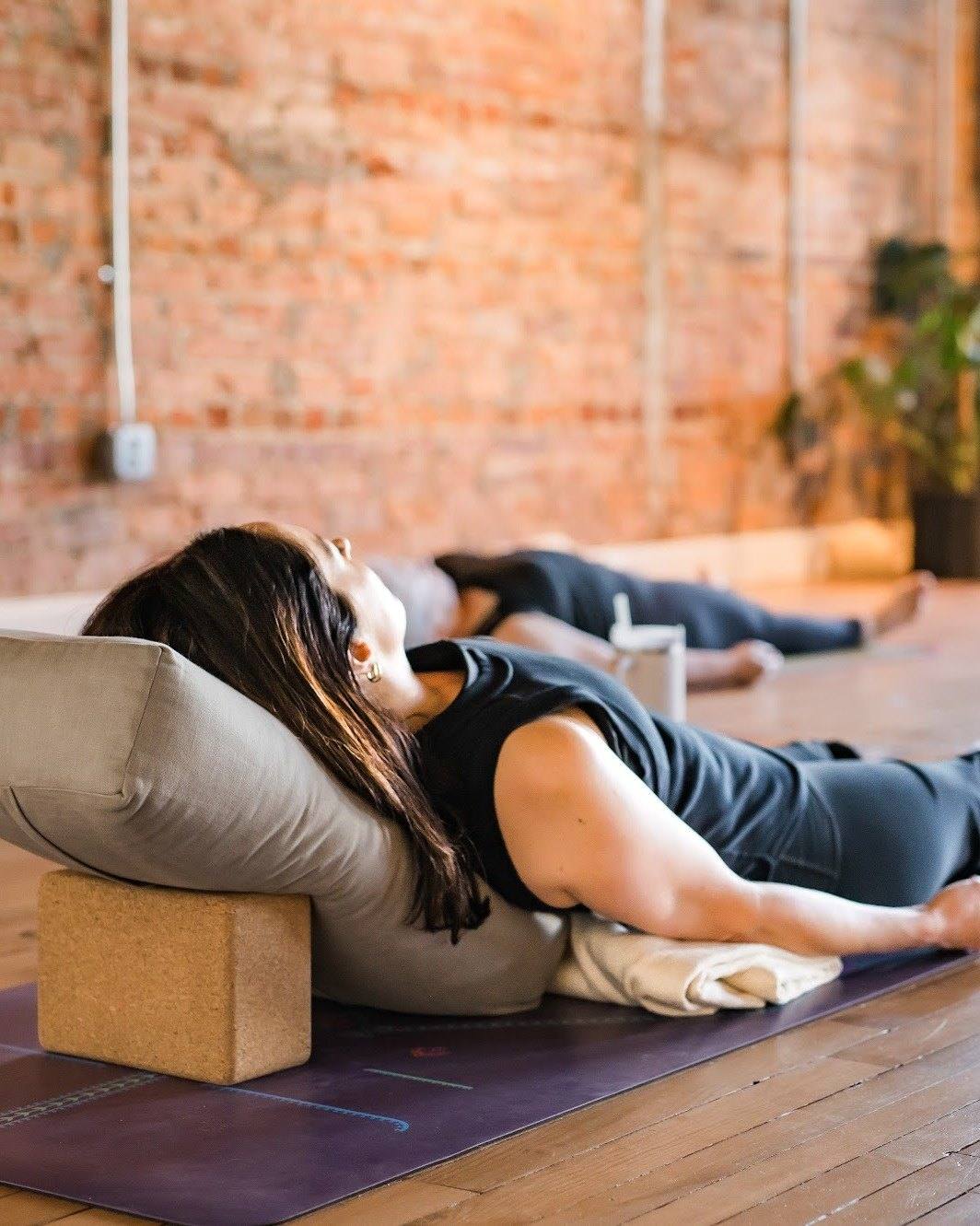 A student resting back over a bolster and block in a restorative pose at The Yoga Loft