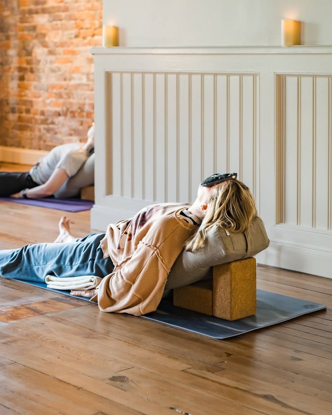 A student resting back over a bolster and blocks in a restorative pose, candles glowing behind