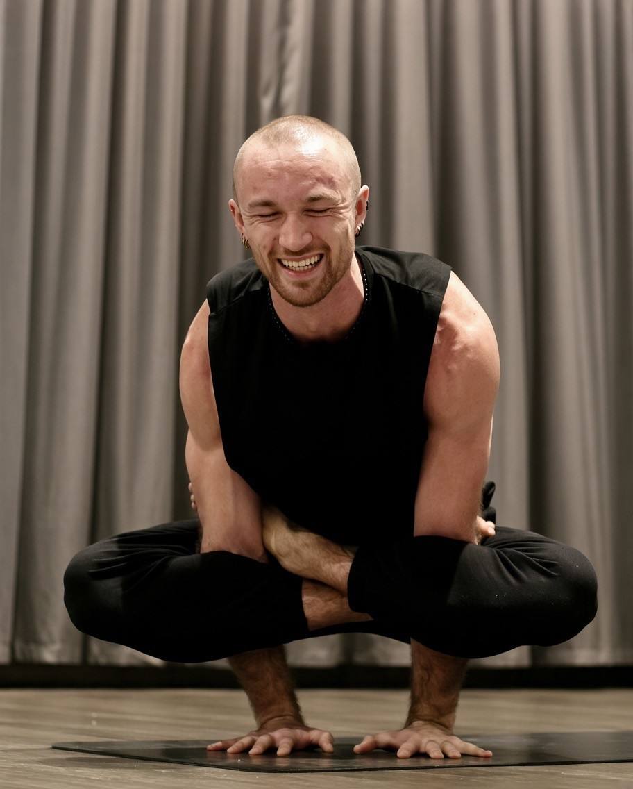 Blaze Gorden smiling in a crow-style arm balance on his mat