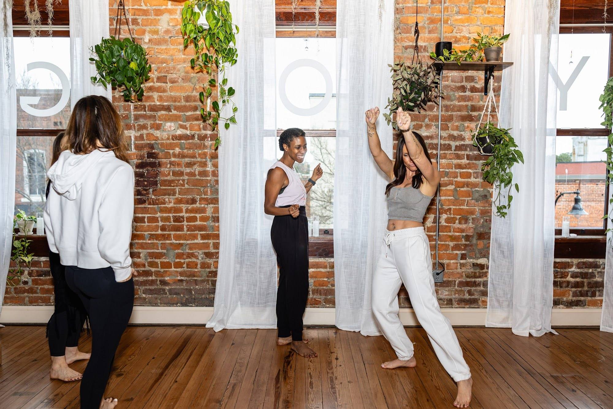 Yoga Loft teachers laughing and dancing by the sunlit windows of the studio
