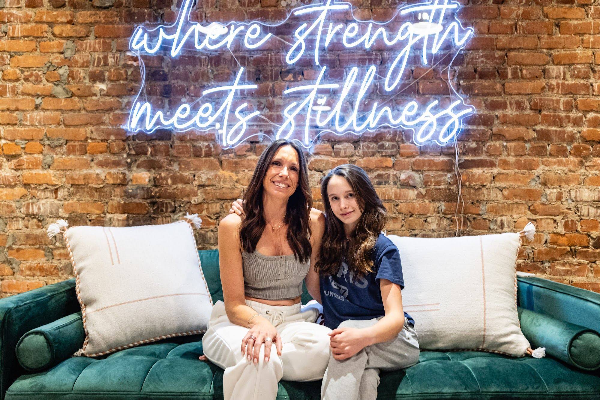 Two teachers laughing together on the sofa under the neon sign