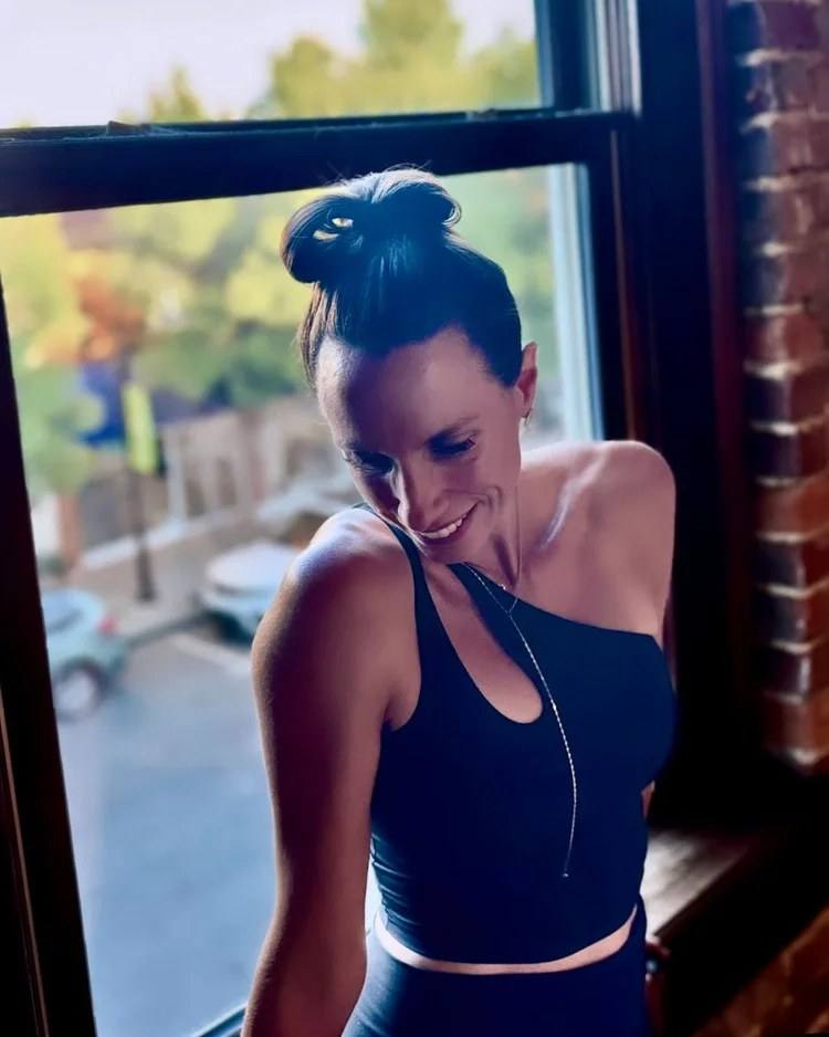 Whitney Carey, founder of The Yoga Loft, smiling by the sunlit studio window above downtown Wake Forest